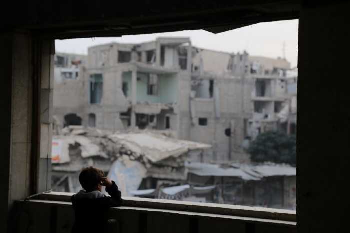 Gutt titter ut av et vindu over ruiner i Syria